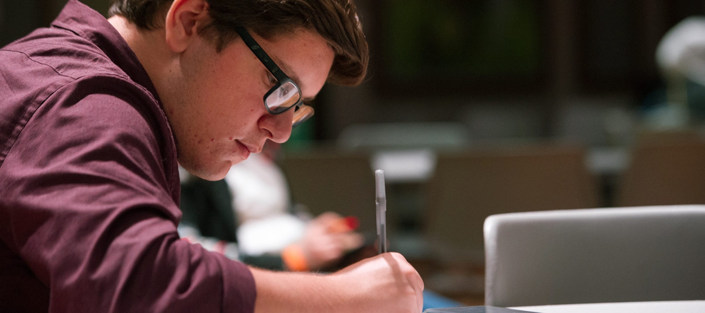 Student writing at a table